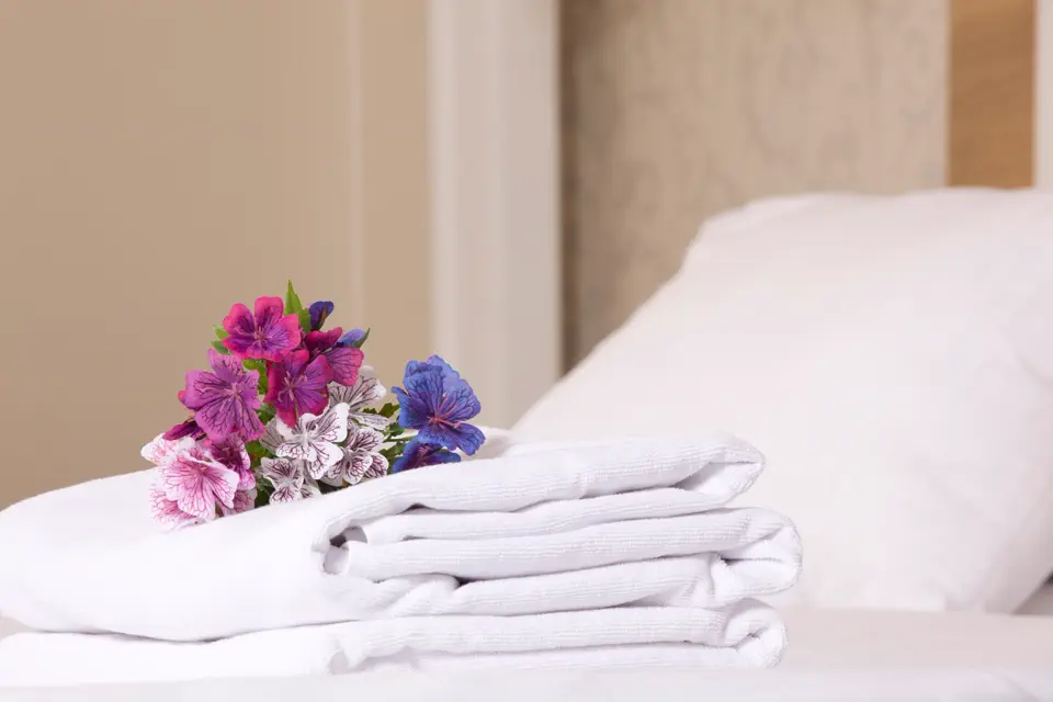 Frisch gefaltete Handtücher und ein Blumenstrauß auf einem bezogenen Bett in einer Ferienwohnung